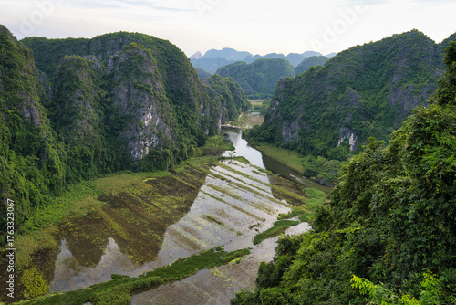 Tableau sur toile Green karst peaks rise around a winding river through a lush valley of rice padd