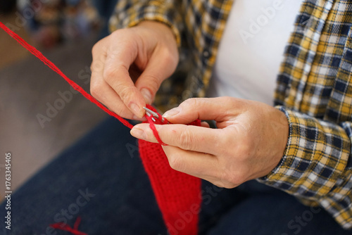 Knitting process of red fabric with needles, close-up of hands with yarn. Concept of hobby, creativity and coziness.