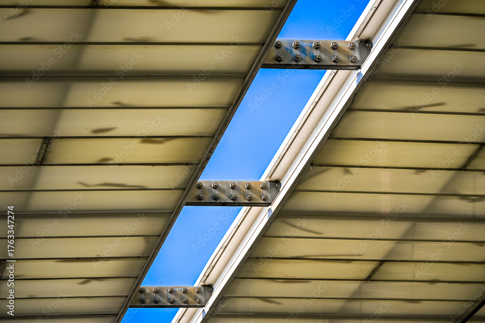 Obraz premium Detail view of a translucent roof made of corrugated panels and metal beams, allowing natural light to filter through the structure.