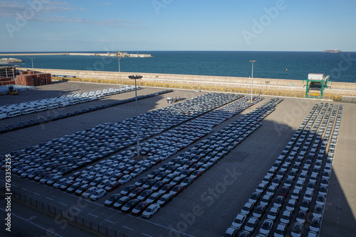 Aerial view of a large car terminal at a seaport, showing rows of new vehicles awaiting export or import