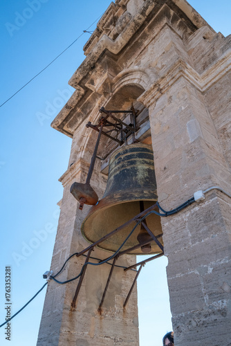 Close-up view of an old bronze church bell mounted in a historic stone bell tower against a clear blue sky.