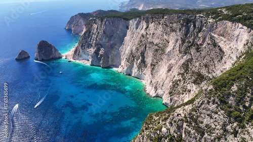 Aerial drone cinematic video of paradise tropical destination island with volcanic caves and white cliffs visited by yachts and sail boats forming a blue lagoon with turquoise crystal clear waters