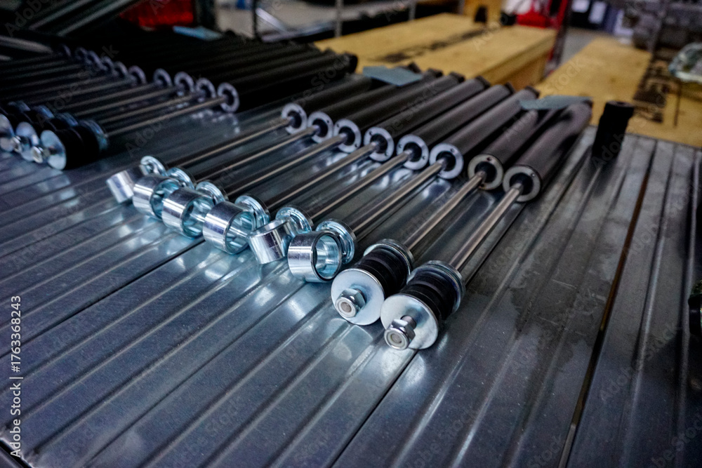 Obraz premium A close-up view of several shiny metal industrial components, possibly nuts or sleeves, lined up on a grooved metal shelf in a factory or warehouse.