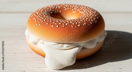 Sesame bagel with overflowing cream cheese. Delicious breakfast pastry on a white wood table. Food photography for menu.
