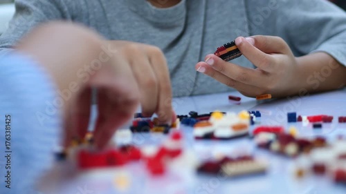 Children hands play with colorful lego blocks on white table.
