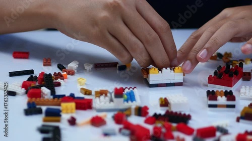 Children hands play with colorful lego blocks on white table.
