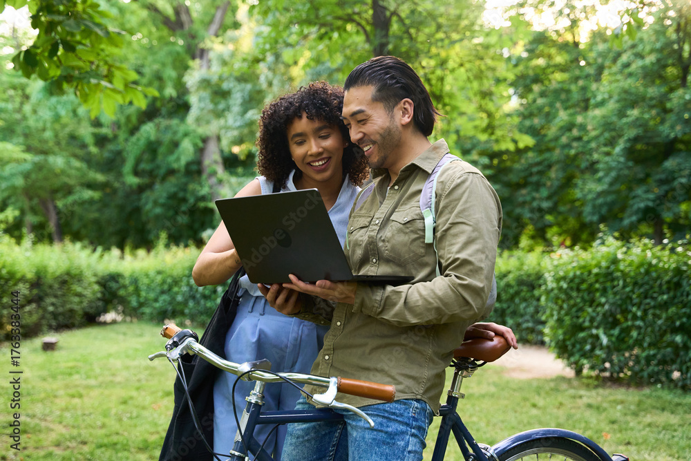 Fototapeta premium Students using laptop next to bicycle in park