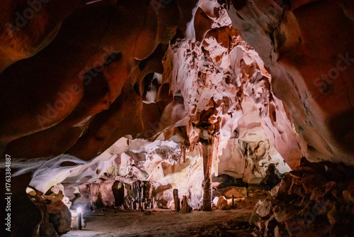 Beautiful view inside Orlova Chuka Cave in Bulgaria, showcasing impressive stalactites and stalagmites illuminated by warm artificial light. The natural rock formations create a stunning abstract patt
