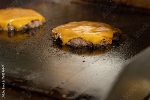 A juicy hamburger patties layered with melted cheddar cheese searing on a hot griddle