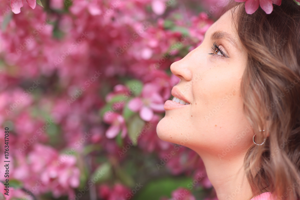 Fototapeta premium Springtime background, a woman in pink in a blooming cherry orchard, a model posing in a romantic style