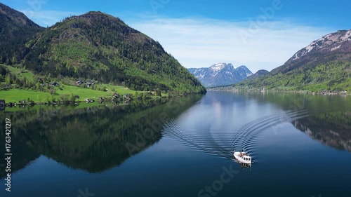 Explore the serene beauty of Grundlsee in Austria with a boat gliding across the tranquil lake. The stunning mountains reflect perfectly in the calm water, capturing a peaceful lakeside scene.