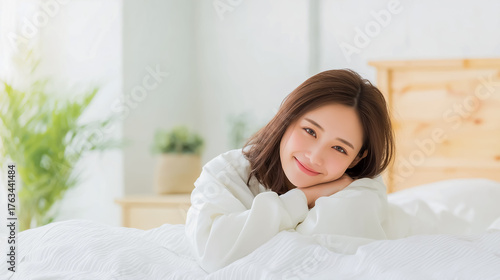 朝の光が差し込むベッドで微笑む若い女性