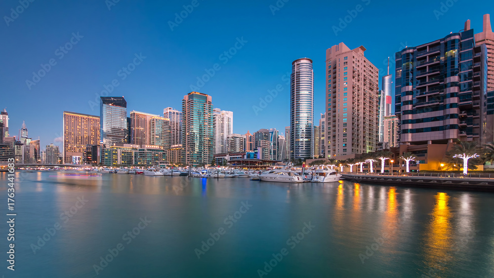 Fototapeta premium Dubai Marina towers and yachts reflected in water of canal in Dubai day to night timelapse