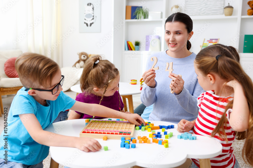 Fototapeta premium Cute children and smiling teacher at white table during lesson in elementary school
