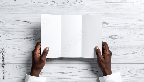 A Person's Hands Holding a Blank Tri-Fold Brochure on a White Wooden Surface