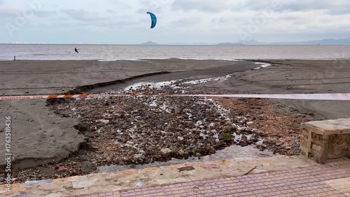 Murcia, Spain - October 12, 2025: Orange Civil Protection tape blocks access to a quiet beach under cloudy skies