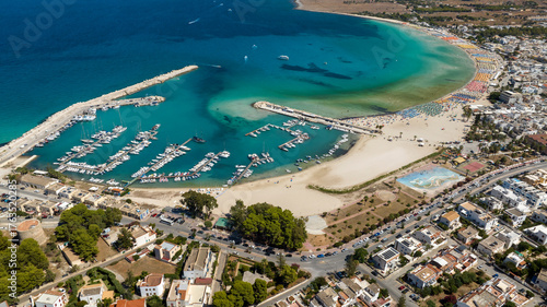 Aerial view of the marina of San Vito Lo Capo, a tourist destination in the province of Trapani, Sicily, Italy. Alongside the harbor, where many boats are docked, lies the sandy beach.