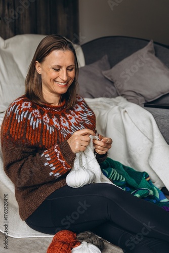 Woman sitting on a sofa and knitting with white yarn. Cozy handmade hobby, relaxation at home, quiet winter activity and creative selfcare concept