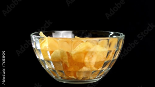 Close-up hand picking potato chips from glass bowl in different ways on black background isolated
