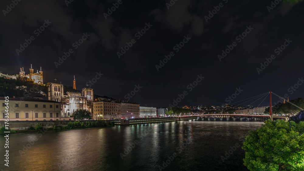 Fototapeta premium Panorama showing night timelapse of Lyon's cityscape with the red suspension footbridge over the Saone River. France