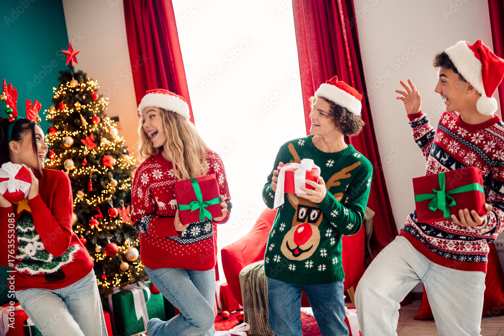 Obraz premium Friends exchanging Christmas gifts in festive sweaters by a decorated tree amidst a cheerful holiday home interior