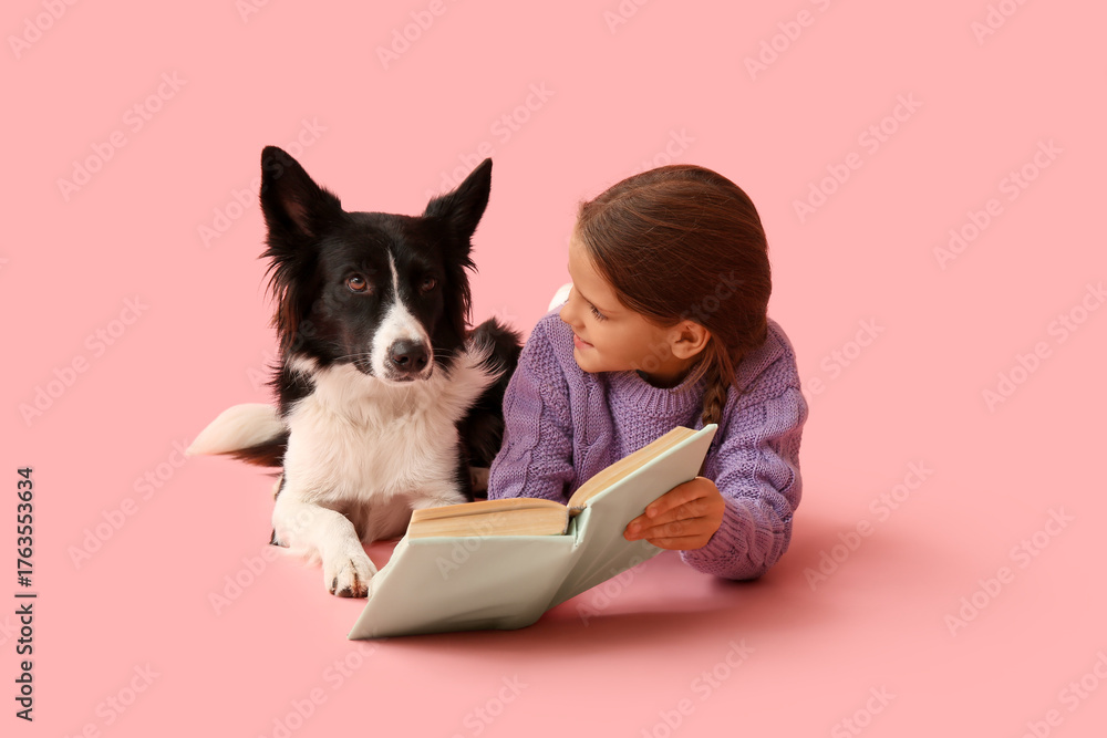 Naklejka premium Cute little girl with Border Collie dog reading book on pink background