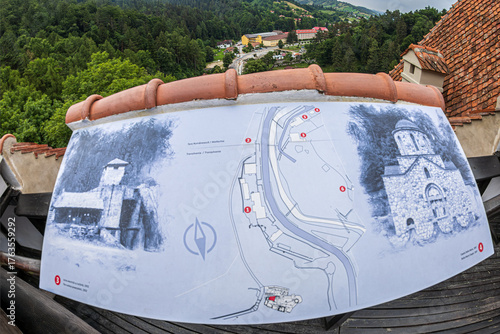 View over Bran village and the surrounding mountains from Dracula's Castle. Informative picture in the foreground, with the old buildings from this view, Bran, Transylvania, Romania