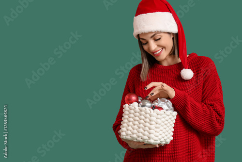 Beautiful woman in Santa hat with Christmas balls on green background