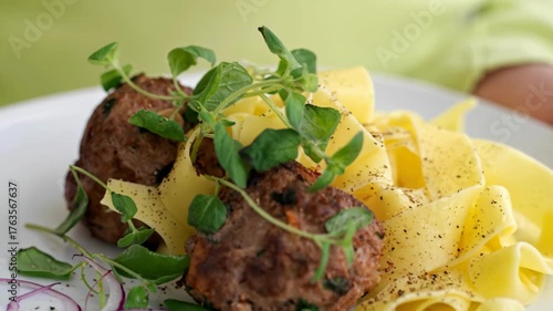 Delicious meatballs served with fresh pasta and herbs on a white plate in a bright kitchen setting.