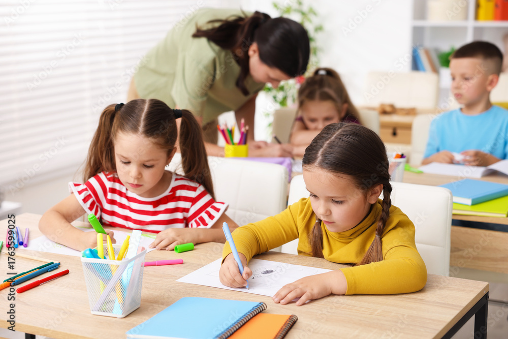 Fototapeta premium Children having lesson with teacher at wooden desks in elementary school