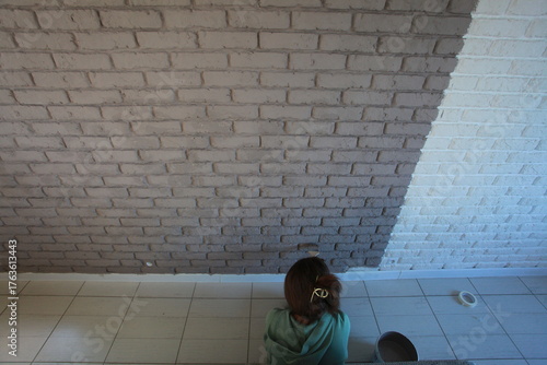 A young woman paints a brick wall with a brush in gray color
