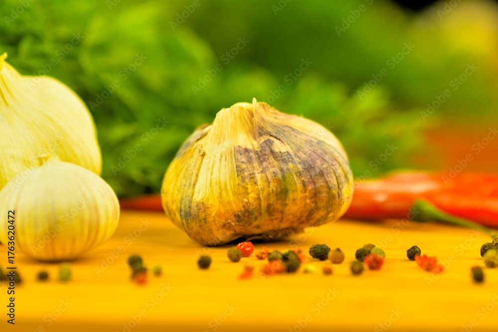 Obraz premium Garlic bulbs, red chili peppers, and four-color peppers on a wooden cutting board. The concept of cooking and vegetables in the home. Garlic - Allium sativum is a species of bulbous flowering plants