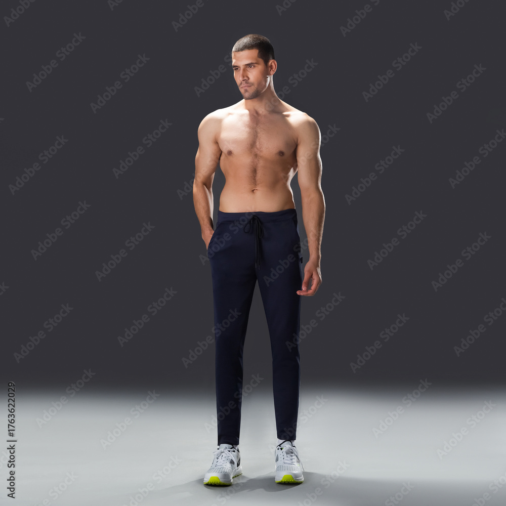 Fototapeta premium athletic male model standing in studio, showing muscular back, shoulders, and fit physique against dark background.