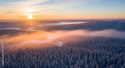 Sunrise over a misty winter forest with snow-covered trees and a vibrant sky.