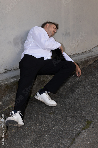 A young businessman, completely drunk, lying on the ground in his white shirt and black trousers.