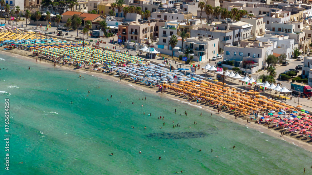 Fototapeta premium Aerial view of umbrellas on the beach of San Vito Lo Capo, a tourist destination in the province of Trapani, Sicily, Italy. It overlooks the Mediterranean Sea and is visited by tourists every summer.