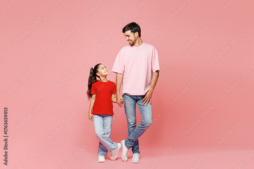 Fototapeta premium Full body young smiling happy parent man with child girl wear red casual clothes. Daddy little kid daughter standing holding hands isolated on plain pink background. Father's Day Love family concept.