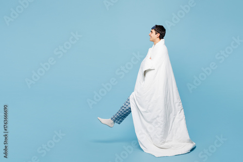 Quadro em tela Full body side profile view calm young man he wear pyjamas jam sleep eye mask rest relax at home be wrapped in blanket duvet walk isolated on plain pastel blue background