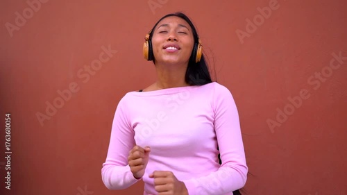 Young indigenous woman dancing to music playlist with wireless headphone in the city - Generation z, technology and lifestyle concept