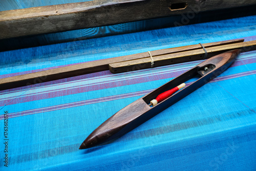 Weaving shuttle with red bobbin on a blue saree. Traditional accessories for handloom weaving.