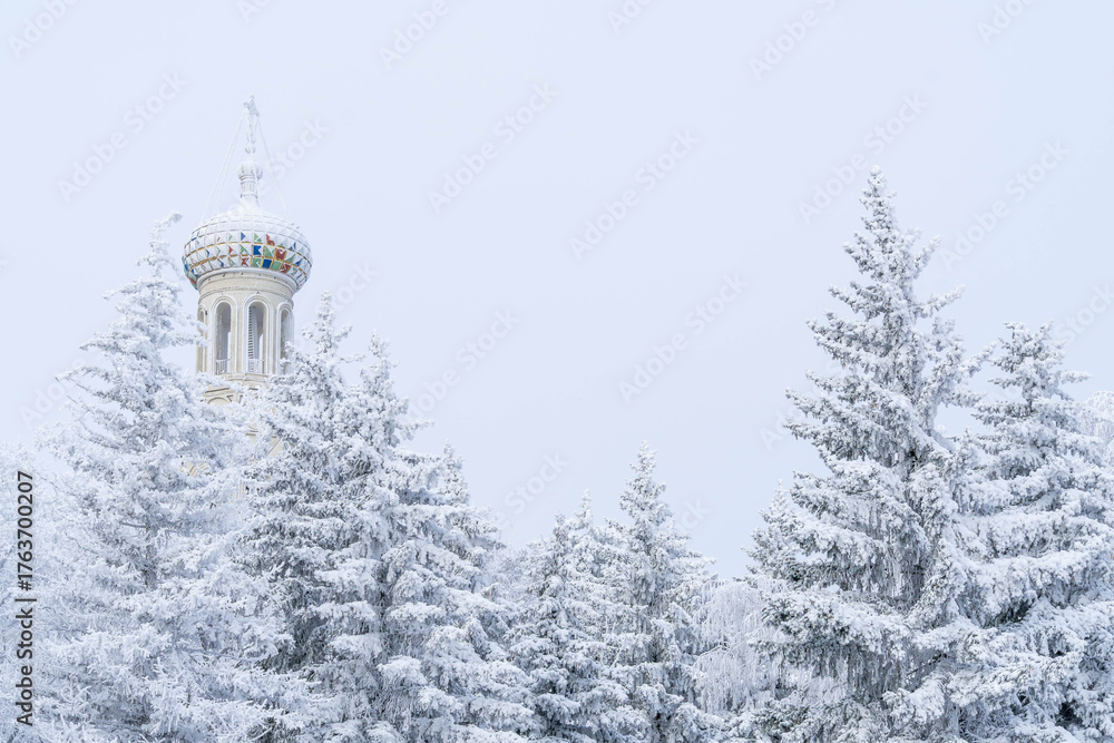 Fototapeta premium Dome of the Kazan Cathedral above snow covered fir trees in Stavropol, Russia, during a cold winter morning. 