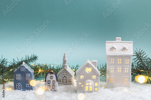 Miniature ceramic houses with festive lights among fir branches, Christmas decoration. Concept of winter holidays and seasonal atmosphere. Christmas background, greeting card.