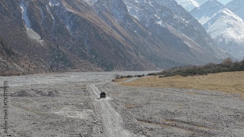 A vehicle navigates through a rugged, rocky landscape, showcasing the expansive valley and towering mountains. The camera follows the vehicle with a smooth dolly motion, enhancing the sense of