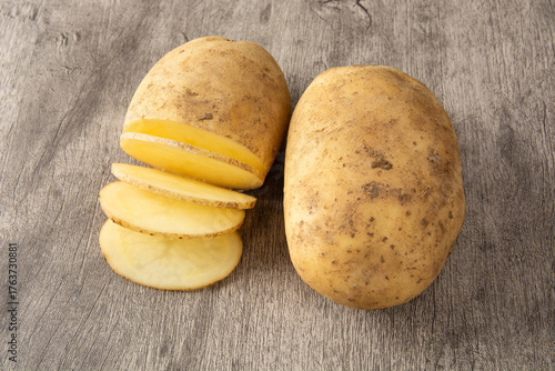 Raw potatoes with slices on a cutting  board over wooden table