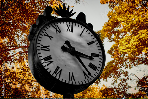 Vintage pocket watch lies on dry yellow leaf and green grass background in autumn fall on ground with sun light. Past time concept, Space for text, Selective focus.