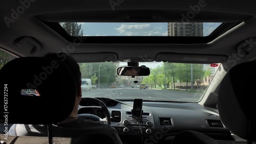 Inside a car a man is driving on a city road on a sunny day