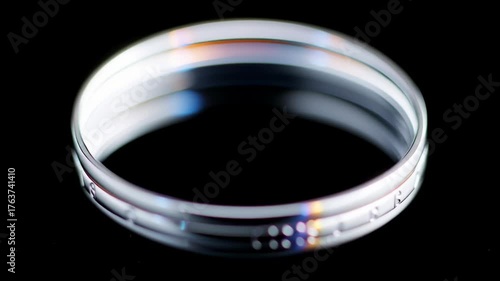 Close up transparent glass petri dish and ring with light reflection and subtle rainbow effect black laboratory science background
