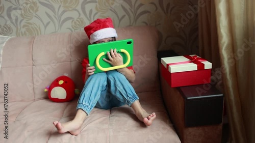 A girl watches a tablet dressed in the Santa hat. New Year's time. A gift for a child.