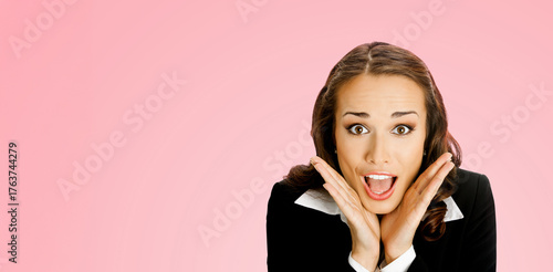Portrait image - surprised businesswoman with expressive eyes open mouth, isolate pink background. Woman wear black business jacket white shirt hands raised to cheeks, astonishment emotion. Free space
