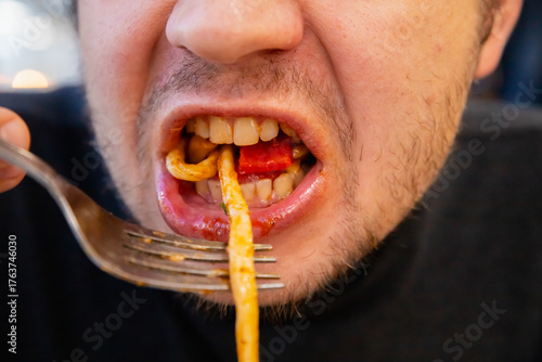 chewing mouth close up view. man eating Lagman noodles, hand holds a fork. Person enjoys a plate of spicy noodles while dining indoors. Gluttony